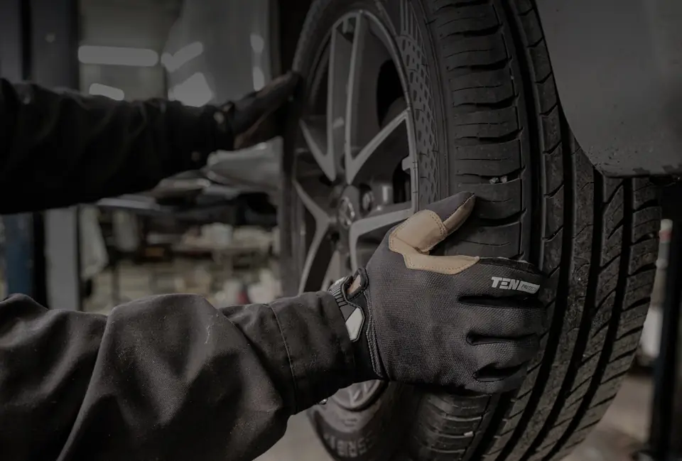 Mechanik v rukavici drží pneumatiku na kolese s alu diskom